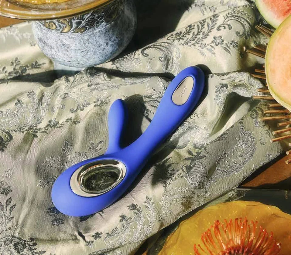 Vibrador Soraya Wave de LELO en azul sobre seda bordada, junto a melón, granada y uvas